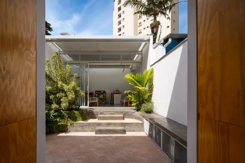 Garden corner: glass sliding doors to the atelier, dense planting, concrete step, neighbouring wall