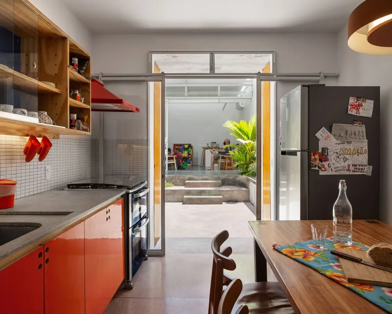 Kitchen: red cabinet doors, timber worktop, open shelving with glass panels, view through to the garden