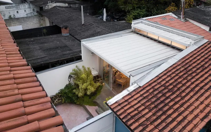 Rooftop view: translucent atelier roof between terracotta tile roofs, courtyard garden below, apartment tower beyond