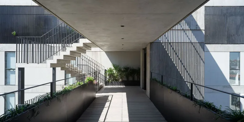 Upper level circulation corridor with concrete planter boxes, vertical steel railings casting shadow patterns on the wall