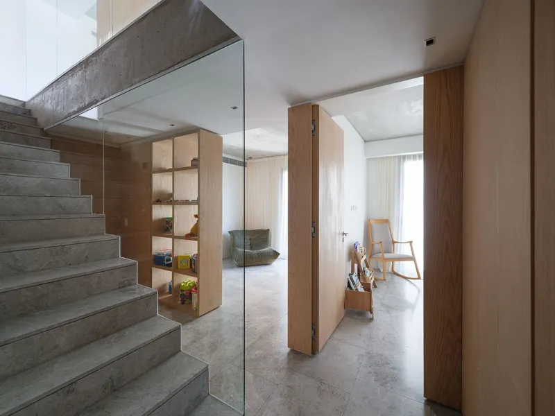 Concrete staircase with glass balustrade alongside timber display shelving unit containing decorative objects and plants