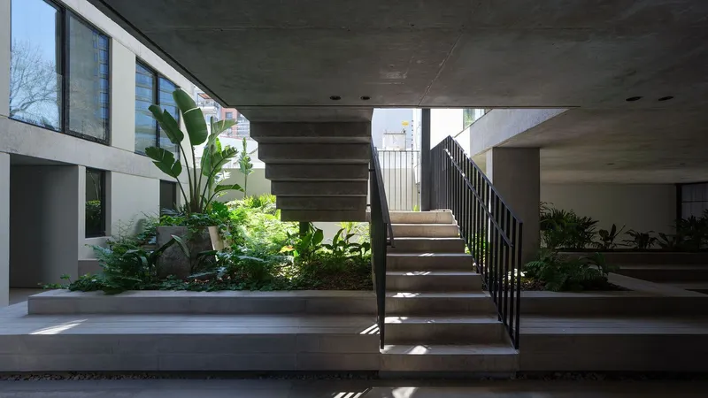 Central staircase with steel railings surrounded by planted beds with banana leaves and tropical vegetation under concrete soffits