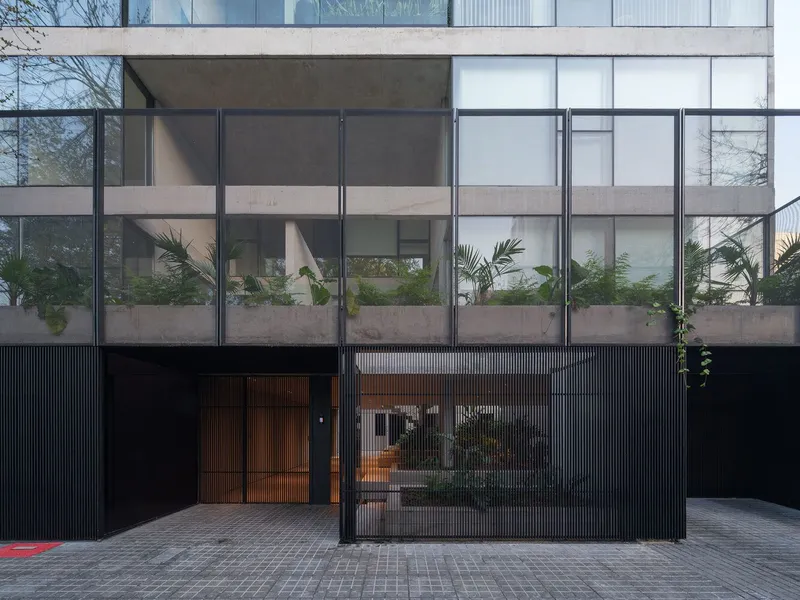 Street facade with black vertical metal cladding, glass balustrades and planted balconies visible behind steel frames