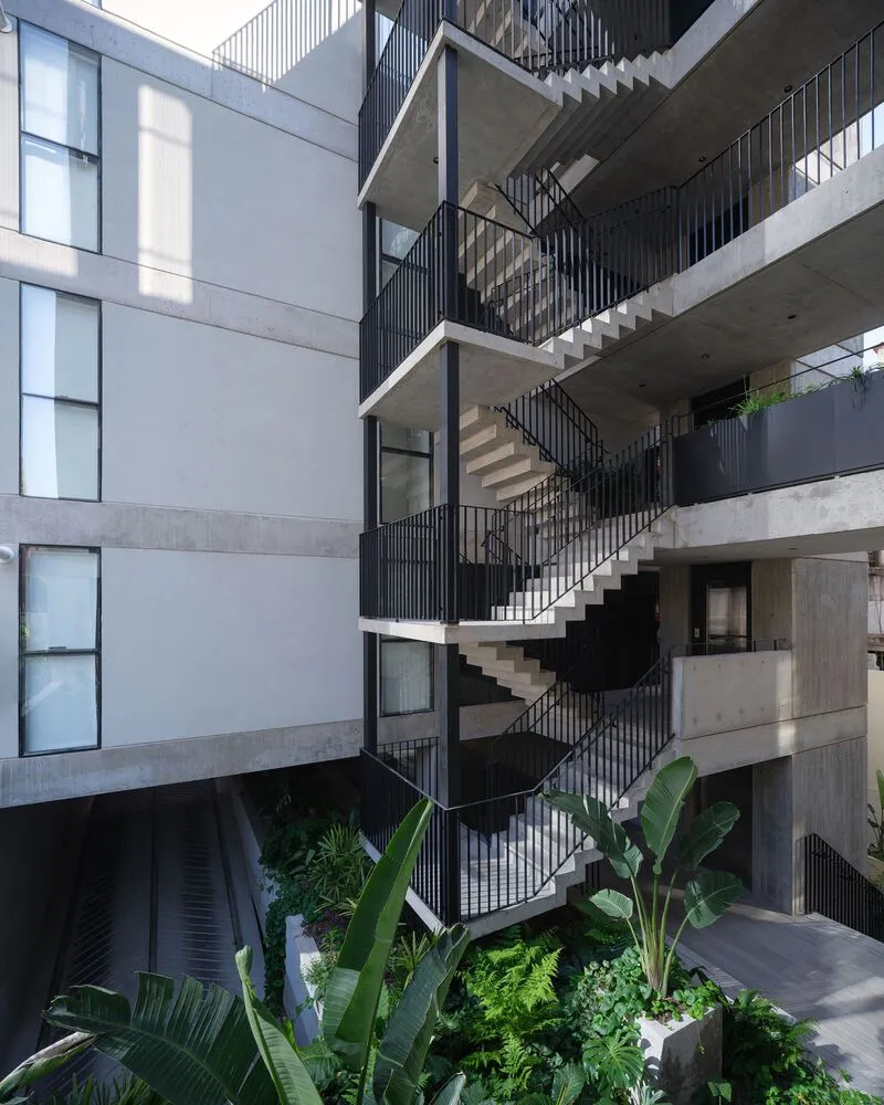 Multi-story interior courtyard with zigzagging concrete staircase, black metal railings, and tropical plantings below