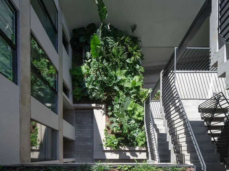 Courtyard view looking up at planted terraces with banana palms and vertical metal screens on concrete balconies