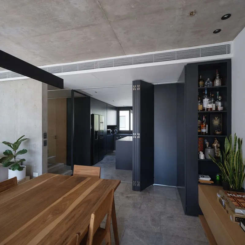 Dining area with timber table, black folding storage wall panels, and recessed open shelving for bottles