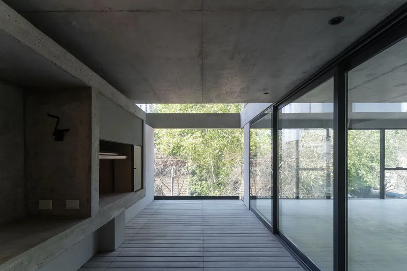 Interior space with exposed concrete ceiling and timber deck looking toward glass walls framing garden vegetation