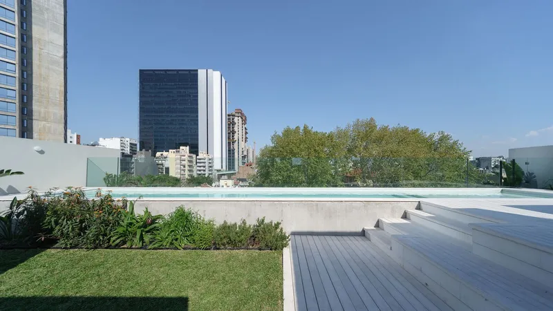 Rooftop terrace with concrete stepped seating, lap pool, and planted lawn overlooking the urban skyline