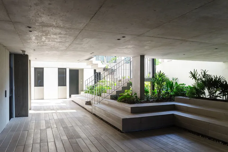 Interior courtyard with stepped timber flooring, exposed concrete ceiling, steel staircase and planted beds with tropical greenery