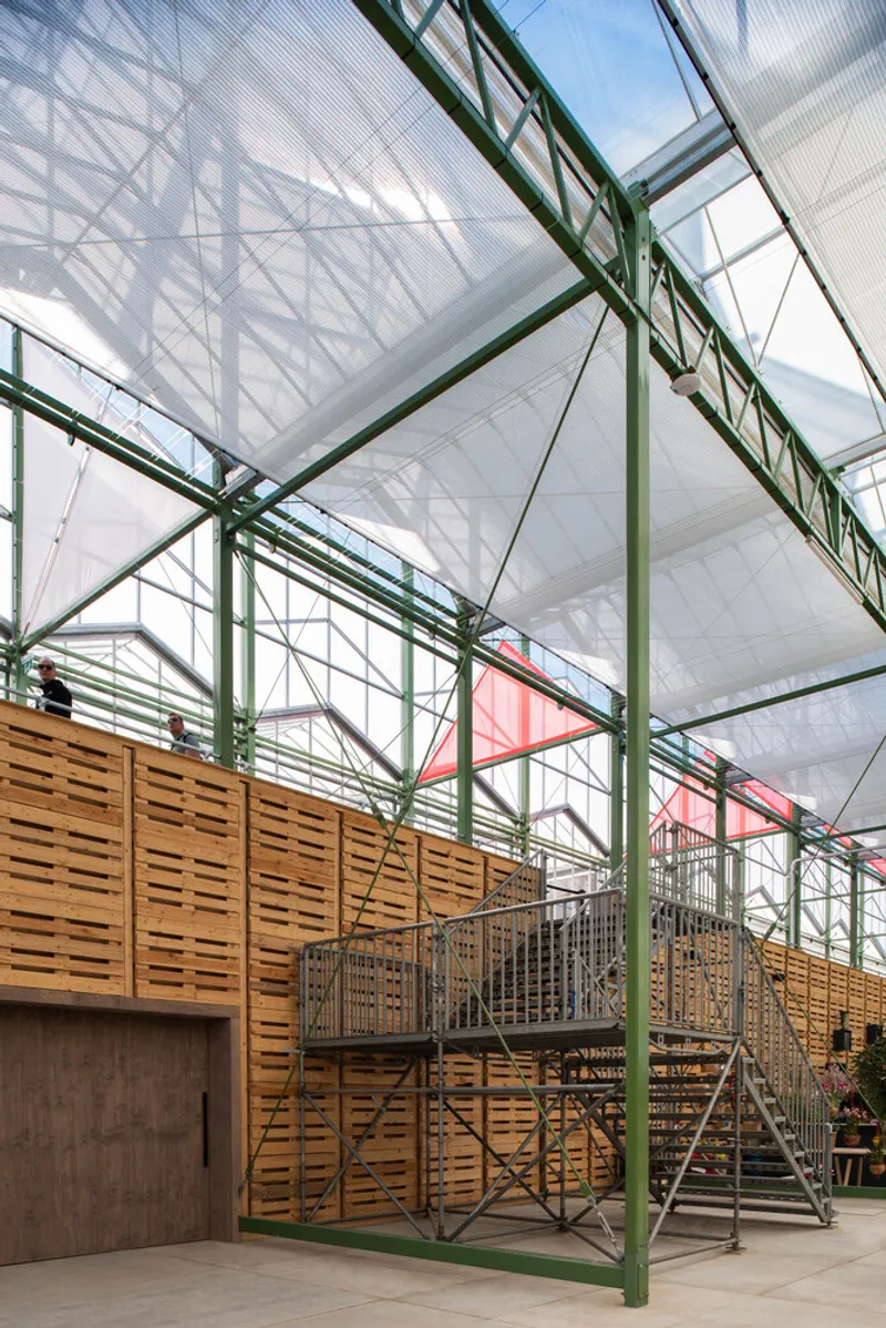 Timber-clad mezzanine with metal stairs beneath green trusses and translucent roof panels inside the greenhouse