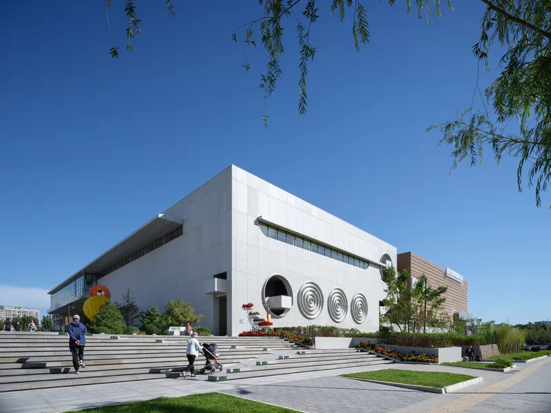 Cultural centre corner: white concrete volume with arched openings, Chinese signage, landscaped steps, pedestrians