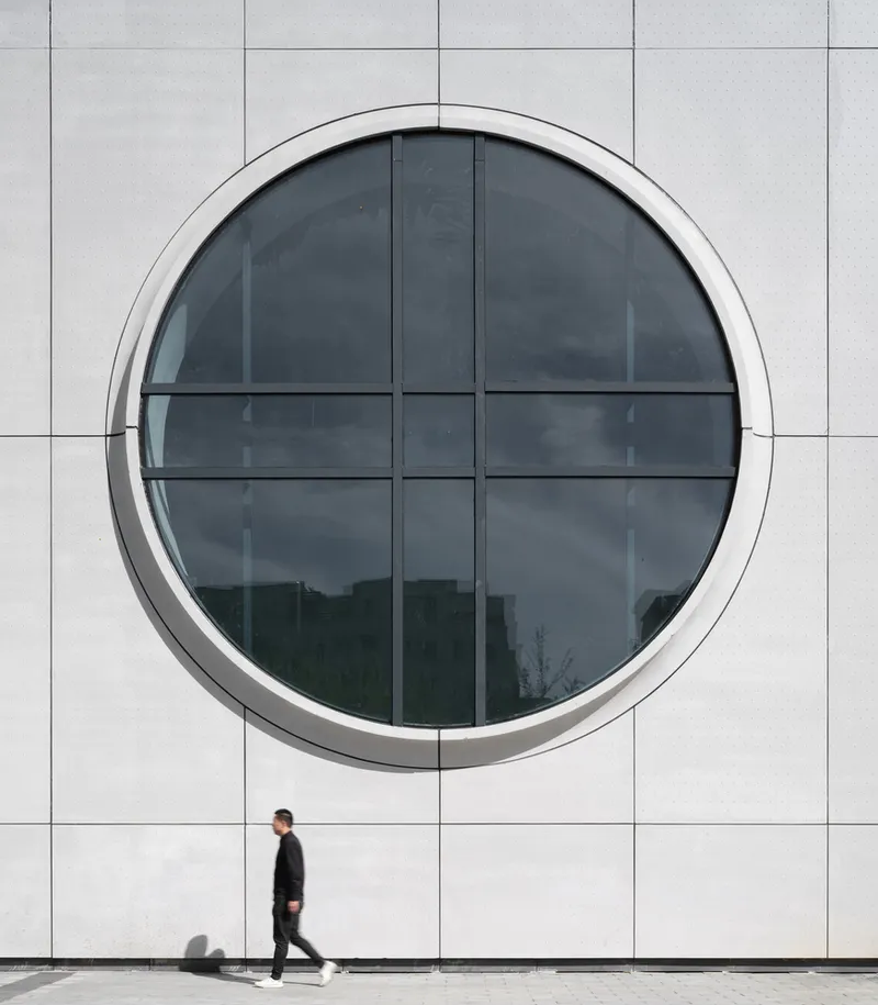 Cultural centre angle: white and brick volumes, circular windows, ground-floor arches, tree canopy