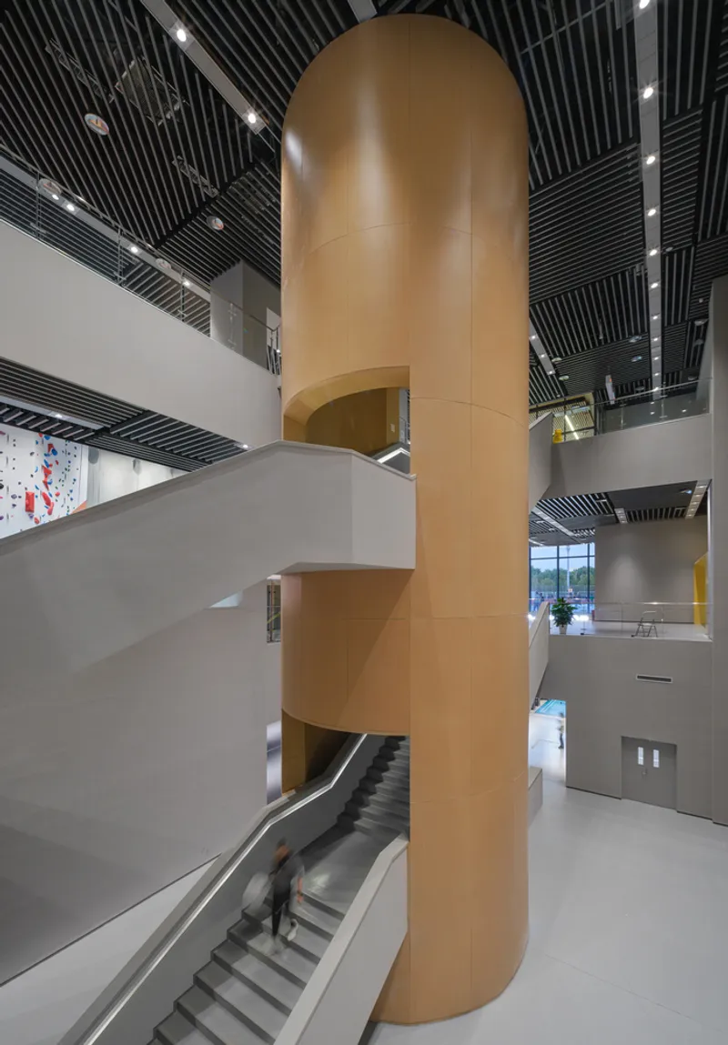 Covered walkway: V-shaped concrete columns supporting timber-clad soffit, cultural centre facade with arched and circular openings beyond