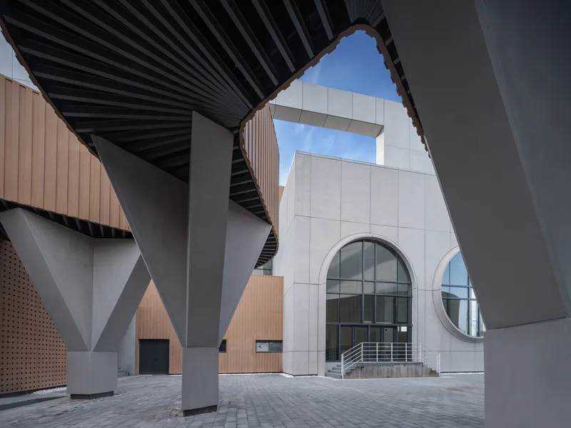 Facade detail: person walking past a large circular glass window in the concrete panel wall
