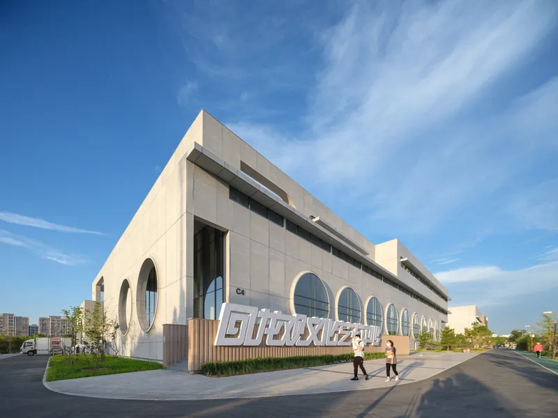 Sports lobby: cylindrical timber-clad column with escalators, exposed steel ceiling grid, coloured wall graphics