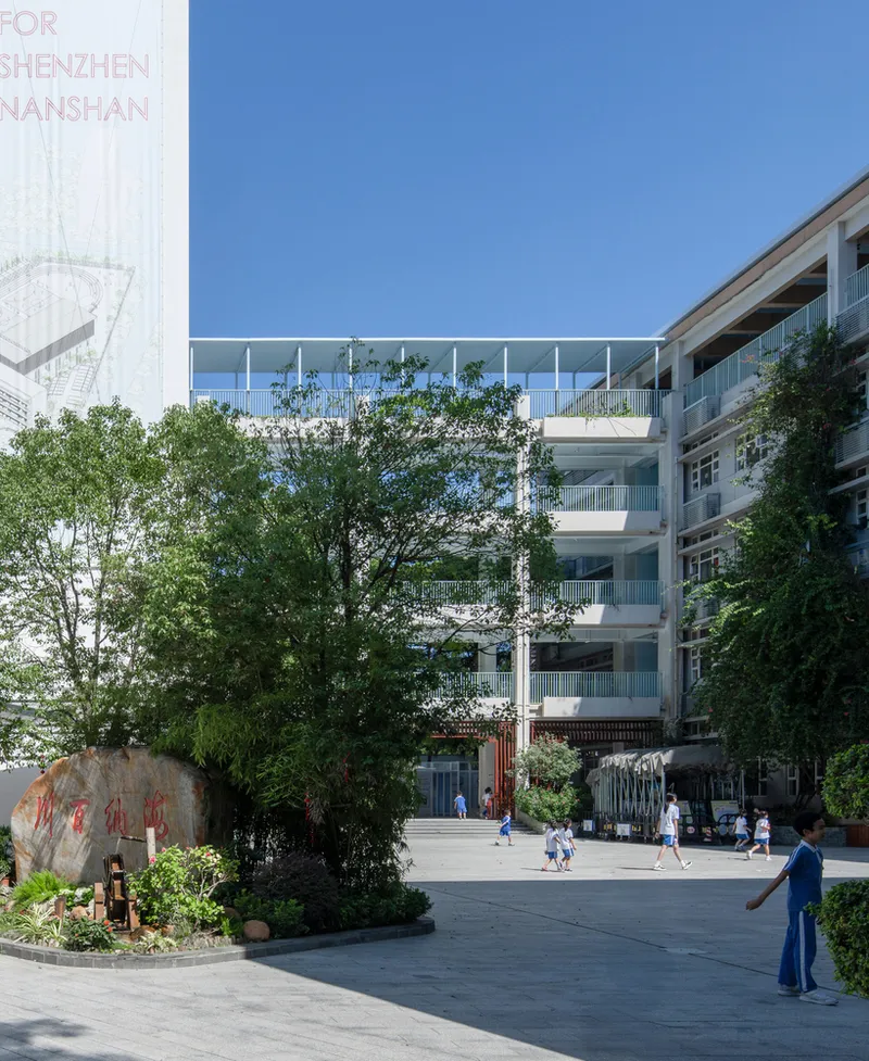 Glass walkway bridge connecting two buildings above a courtyard with trees and students
