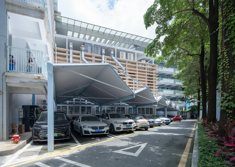 Carport structure with a faceted metal canopy supported by white columns and timber screening above