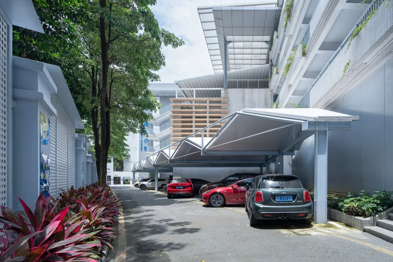 Covered parking area with a folded metal canopy and parked cars beside planted beds