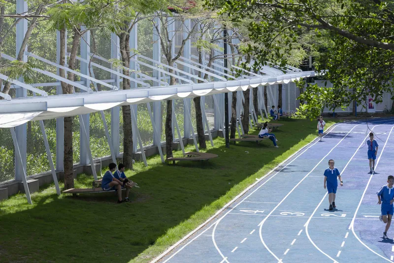 Perforated metal screen wall and undulating fabric shade structure beside the curved running track with students