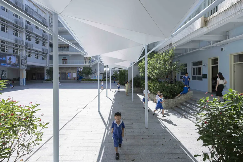 Covered walkway with white steel frame and translucent canopy connecting school courtyard buildings with children passing through