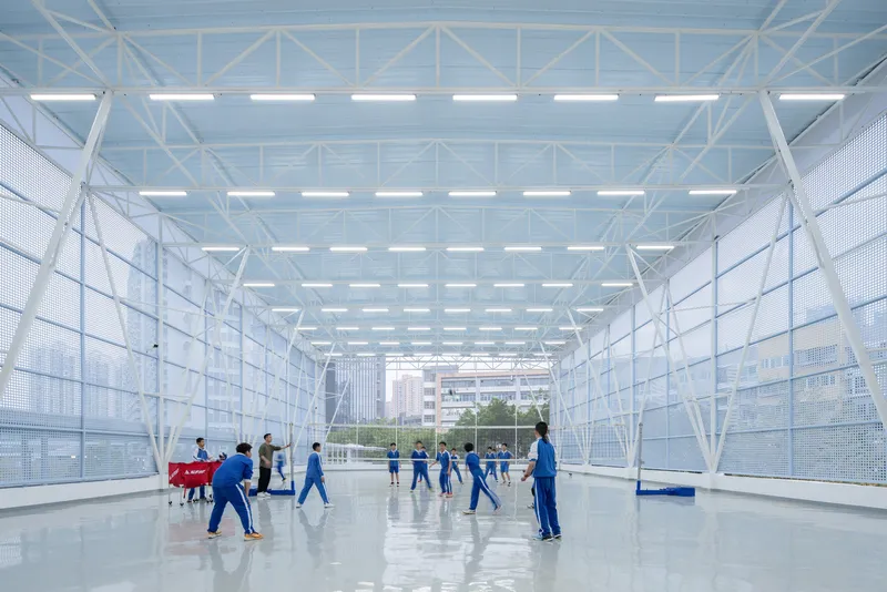 Interior sports court with students playing under linear ceiling lights and perforated mesh walls