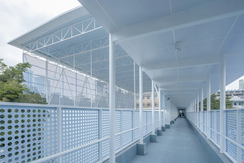 Covered walkway with perforated metal railings and white columns beneath an exposed truss roof structure