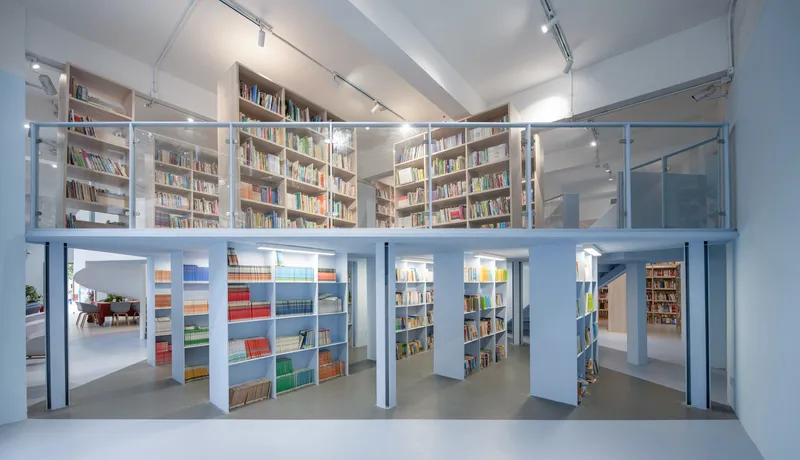 Two-story library interior with mezzanine bookshelves and steel columns viewed from the upper level