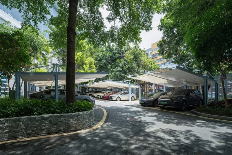 Fabric shade canopies over parking spaces framed by trees and dappled sunlight
