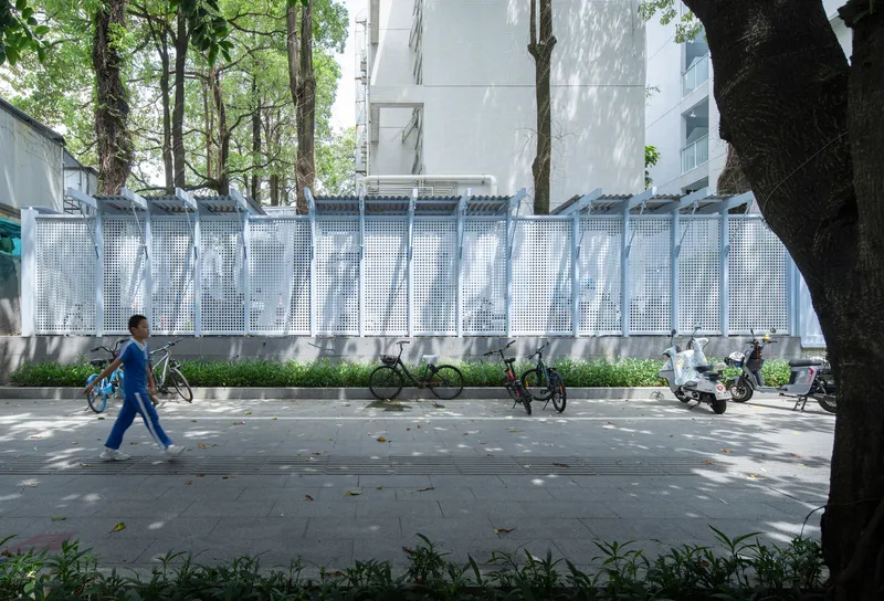 White perforated metal fence along the sidewalk with a person walking past bicycles and trees