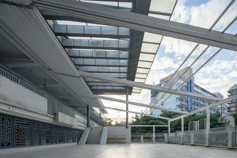 Open-air courtyard with retractable glass and steel canopy above a light-colored paved terrace at dusk