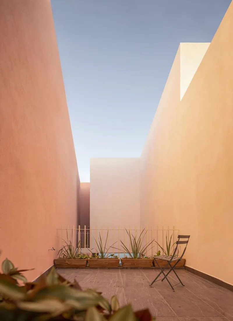 Narrow courtyard framed by peach and orange rendered walls with potted agaves and a folding chair