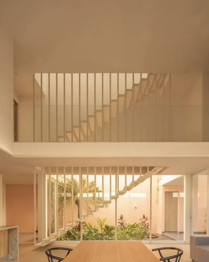 Double-height dining area with vertical slat staircase overlooking a planted courtyard through floor-to-ceiling glazing
