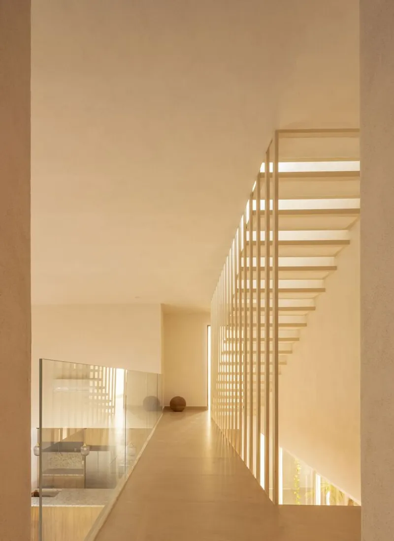 Upper level corridor with vertical timber slat balustrade filtering daylight onto pale stone flooring