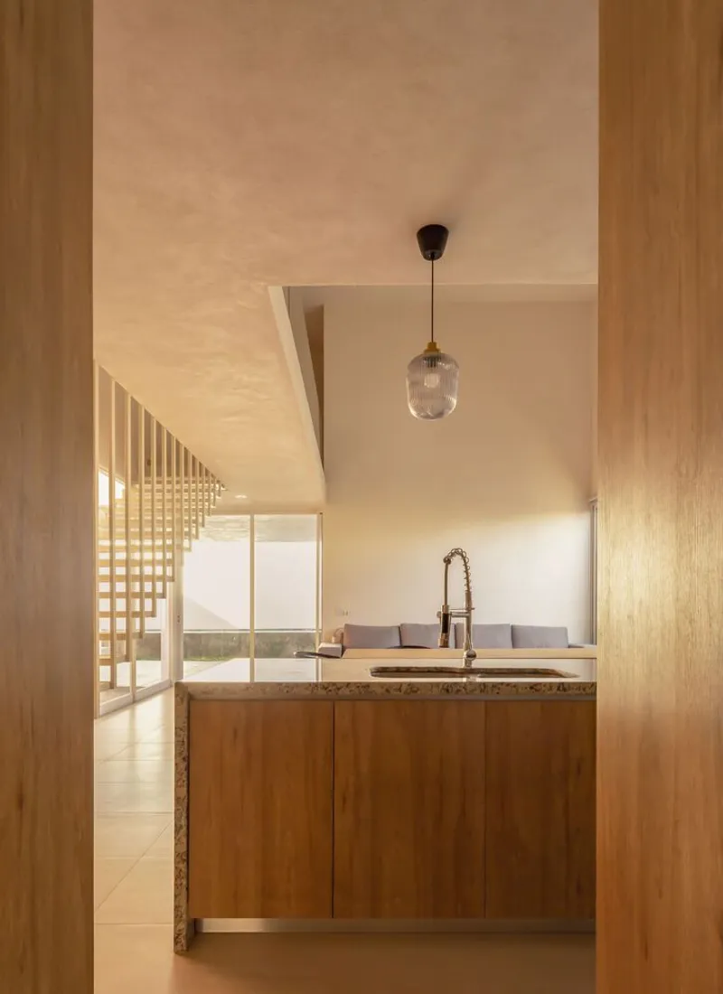 Open kitchen with timber cabinetry and stone countertop viewed through a doorway with pendant light above