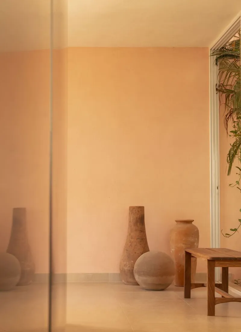 Warm peach-toned interior corner with ceramic vessels and a low wooden table beside a glazed door
