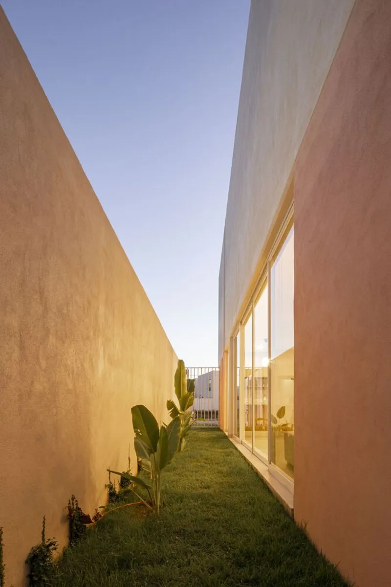 Narrow side courtyard with grass lawn between ochre stucco walls and a glazed facade at dusk
