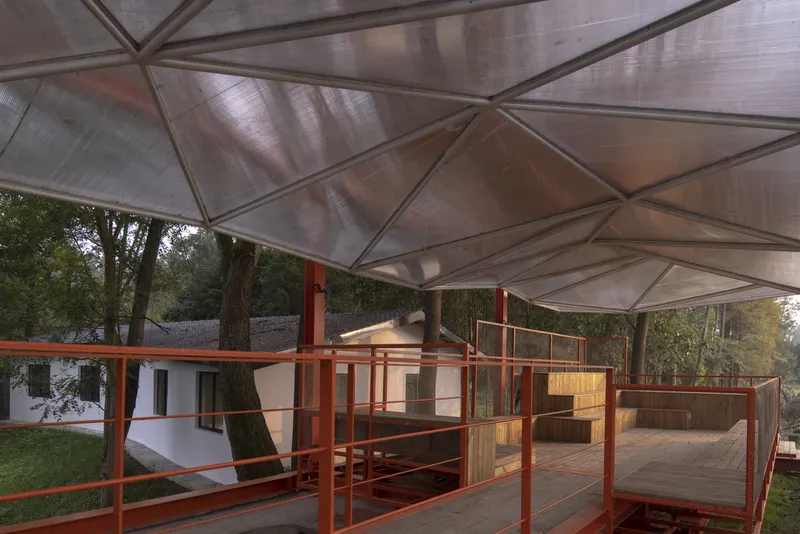 Upper deck: translucent triangular canopy panels overhead, orange steel columns and railings, timber deck, trees visible through the open sides