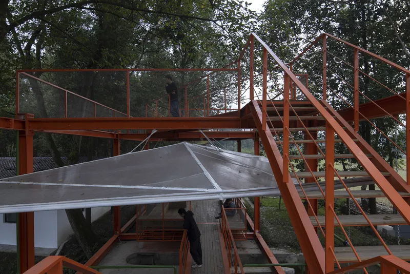 Stair detail: orange steel stair leading to the upper deck, translucent canopy panels above, figure seated below on the timber platform