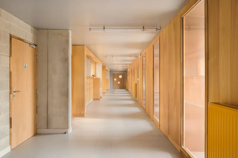 Interior corridor: plywood-lined walls and doors, exposed concrete structure, long perspective, yellow radiator accent