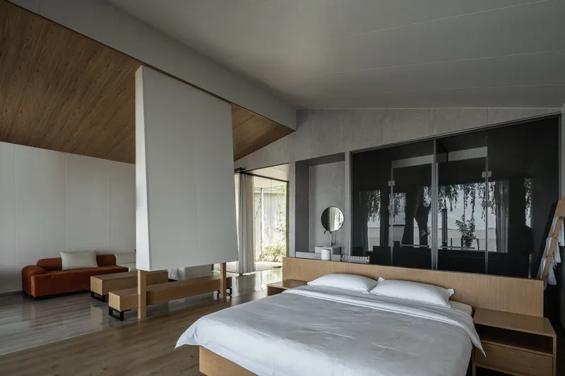 Bedroom with timber ceiling insert, concrete walls, and black framed glazing reflecting garden foliage