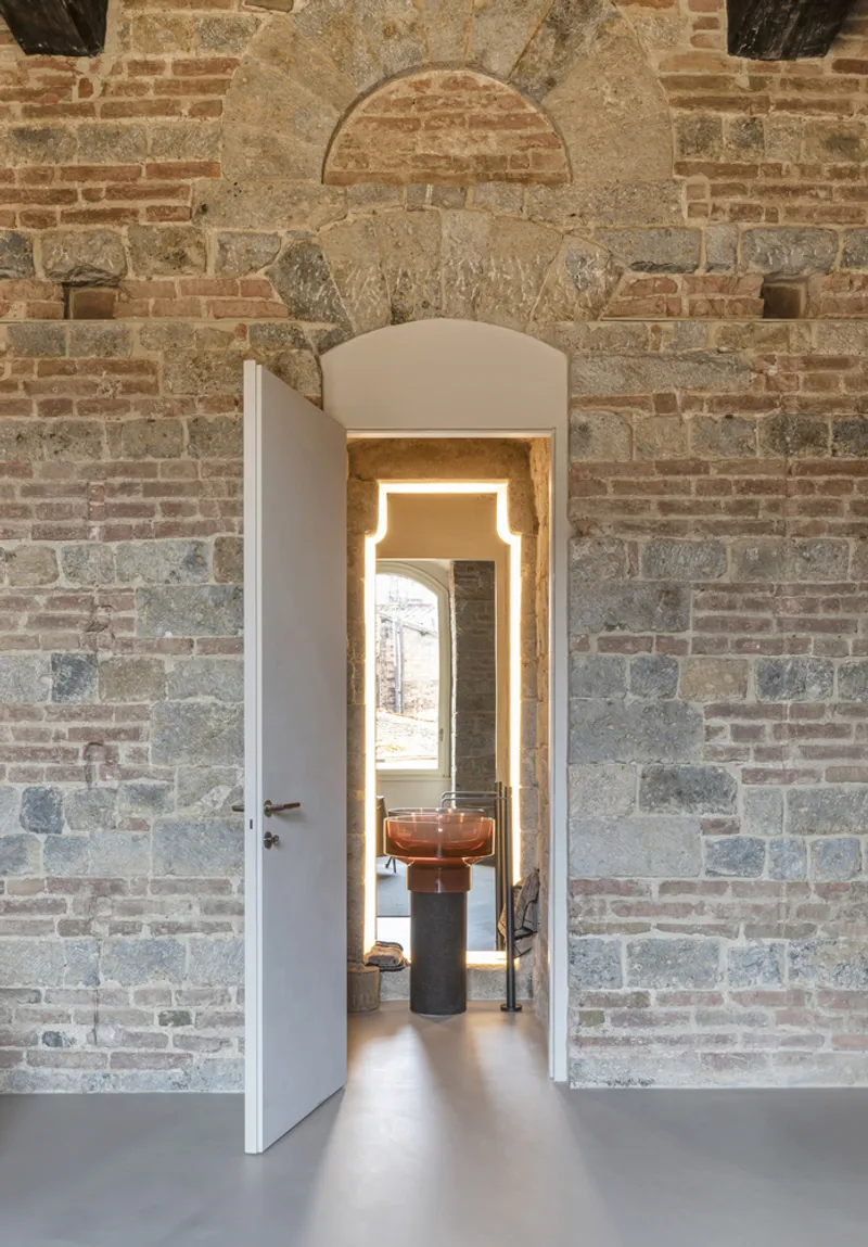Arched doorway cut through brick wall revealing a corridor with copper vessel on pedestal