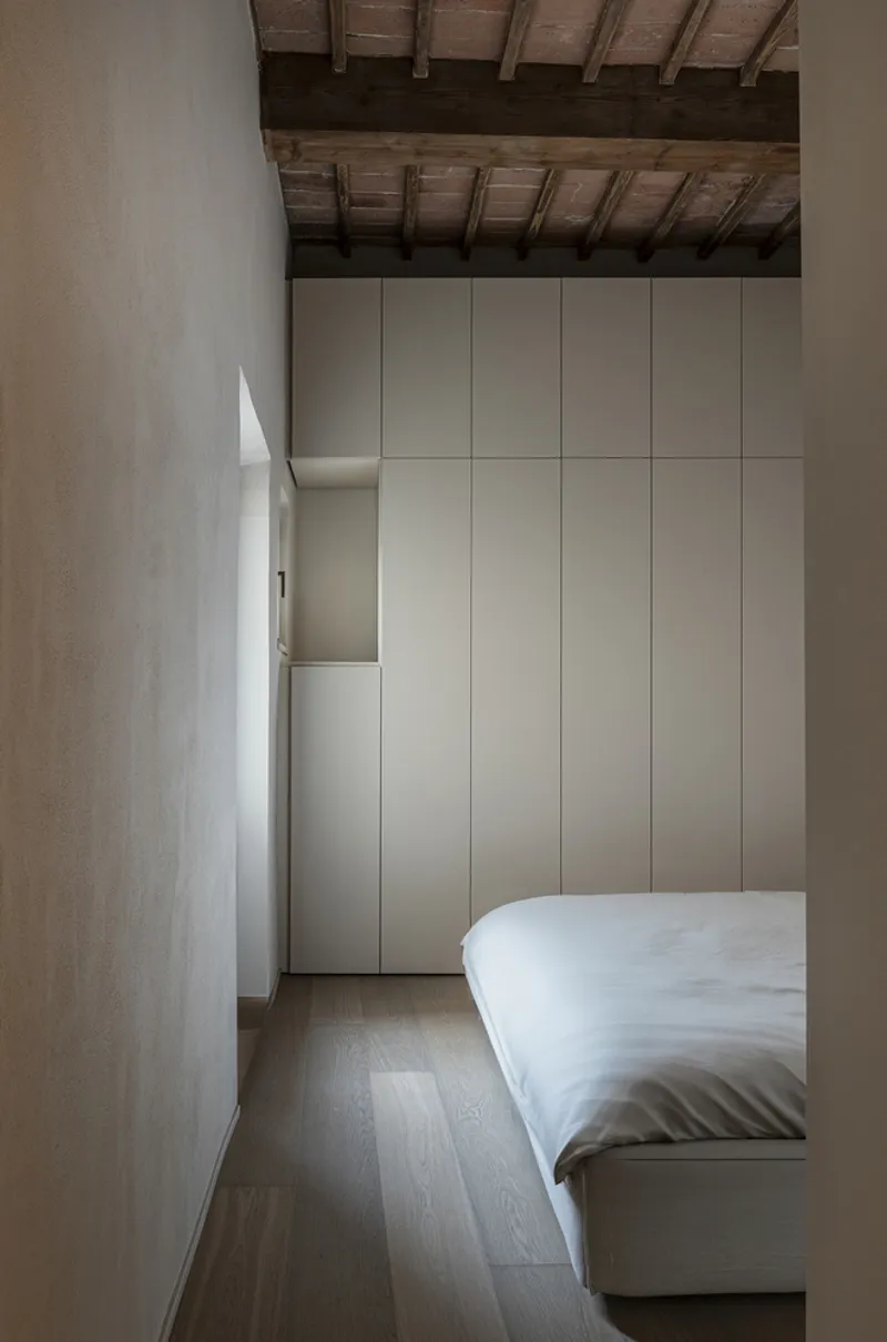 Bedroom with floor-to-ceiling white paneled storage beneath exposed timber ceiling beams