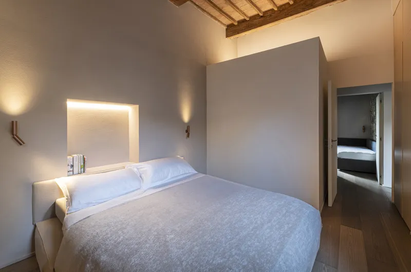 Bedroom with backlit headboard and freestanding partition wall beneath original timber ceiling