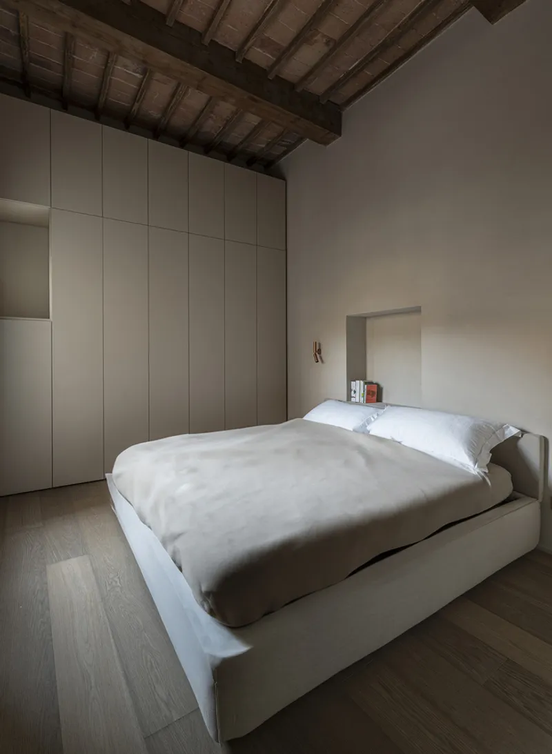 Bedroom with white upholstered bed and recessed wall niche under restored timber roof structure