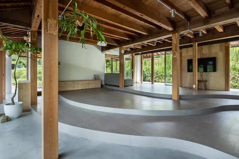 Open interior with exposed timber columns and beams above curved grey flooring and hanging plants