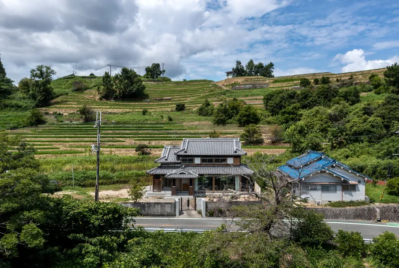 Elevated view of the tiled-roof structure beside a road with terraced hillside fields beyond