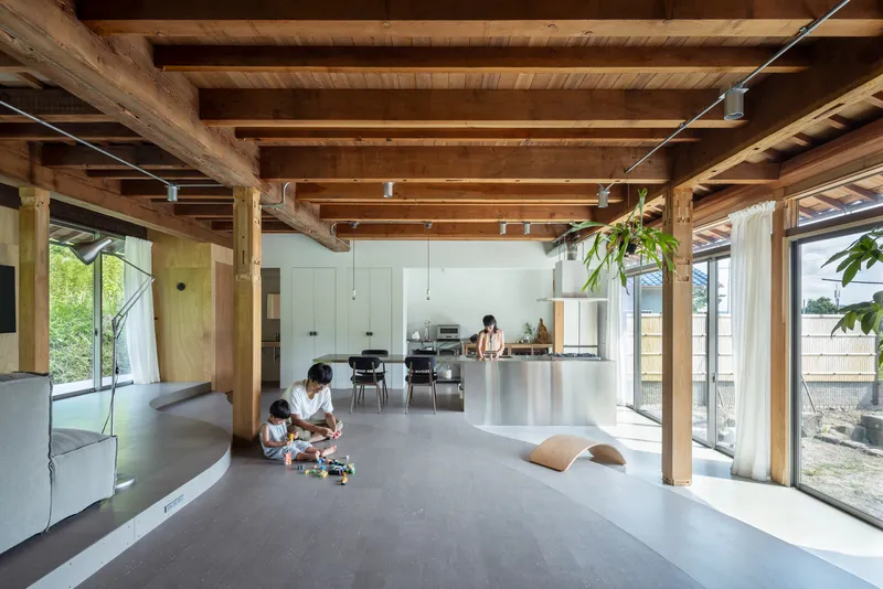 Living space with exposed timber structure and kitchen counter where children play on grey flooring