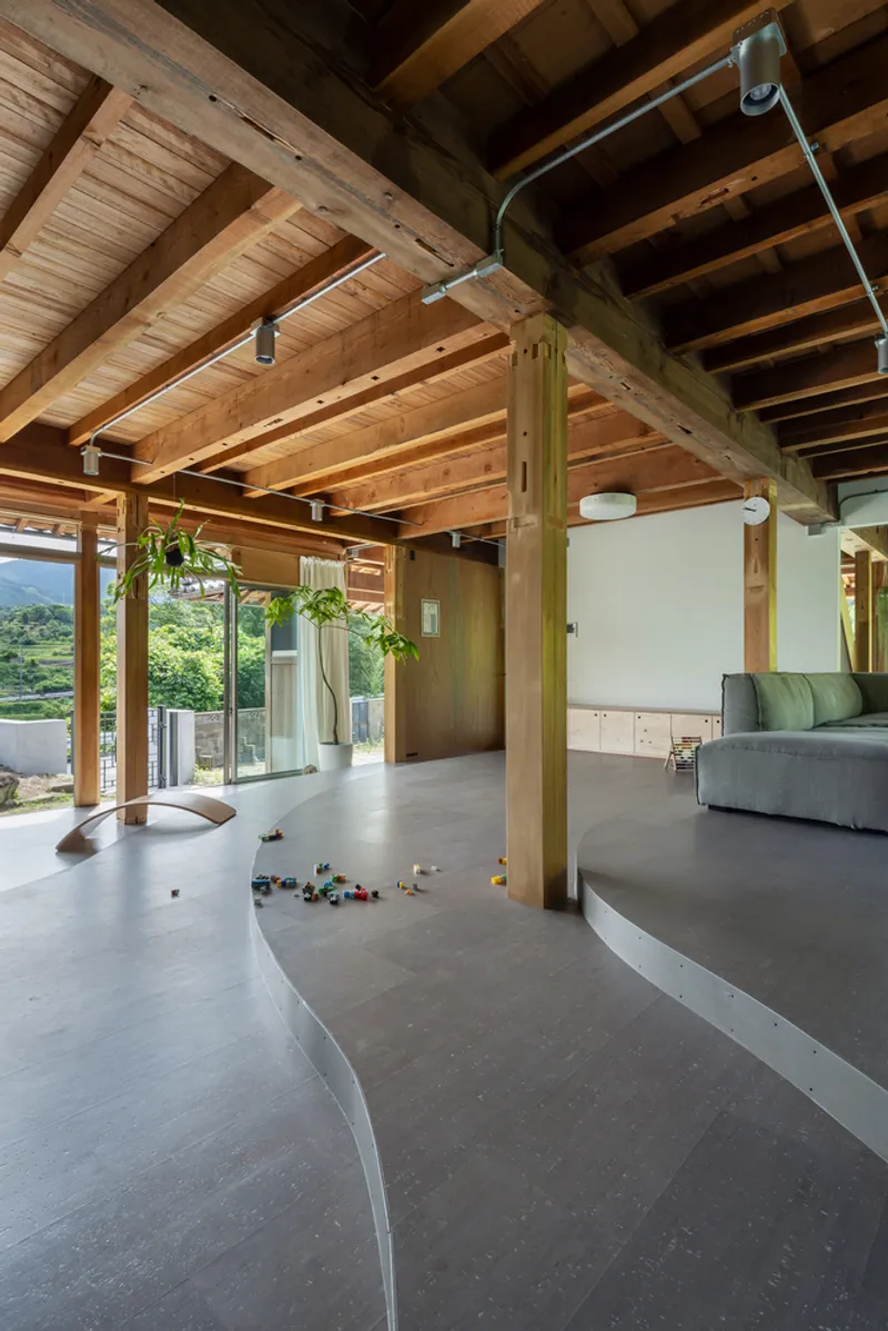 Open-plan interior with exposed timber ceiling beams, polished concrete floor and full-height glazing overlooking green hills