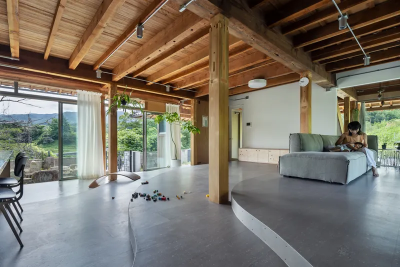 Living space with curved concrete floor level and timber post-and-beam structure, person reading on sofa