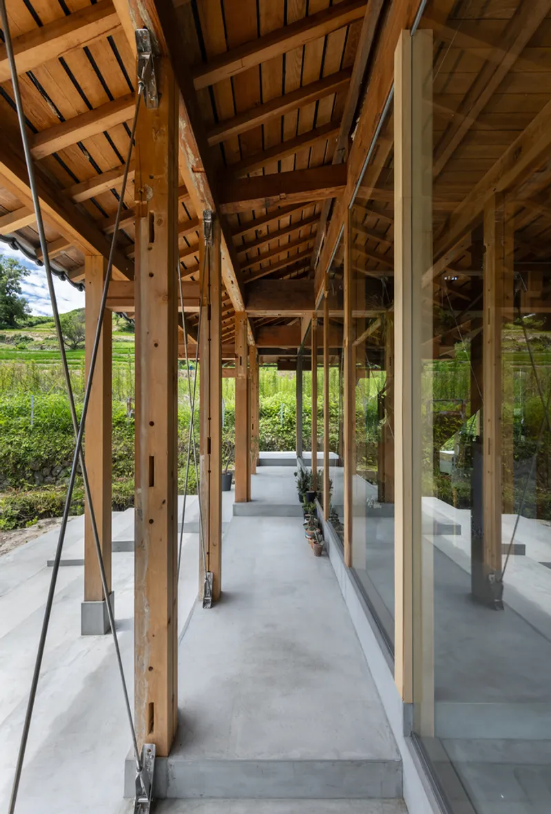 Covered porch with exposed timber rafters, diagonal bracing and full-height glass doors facing planted beds